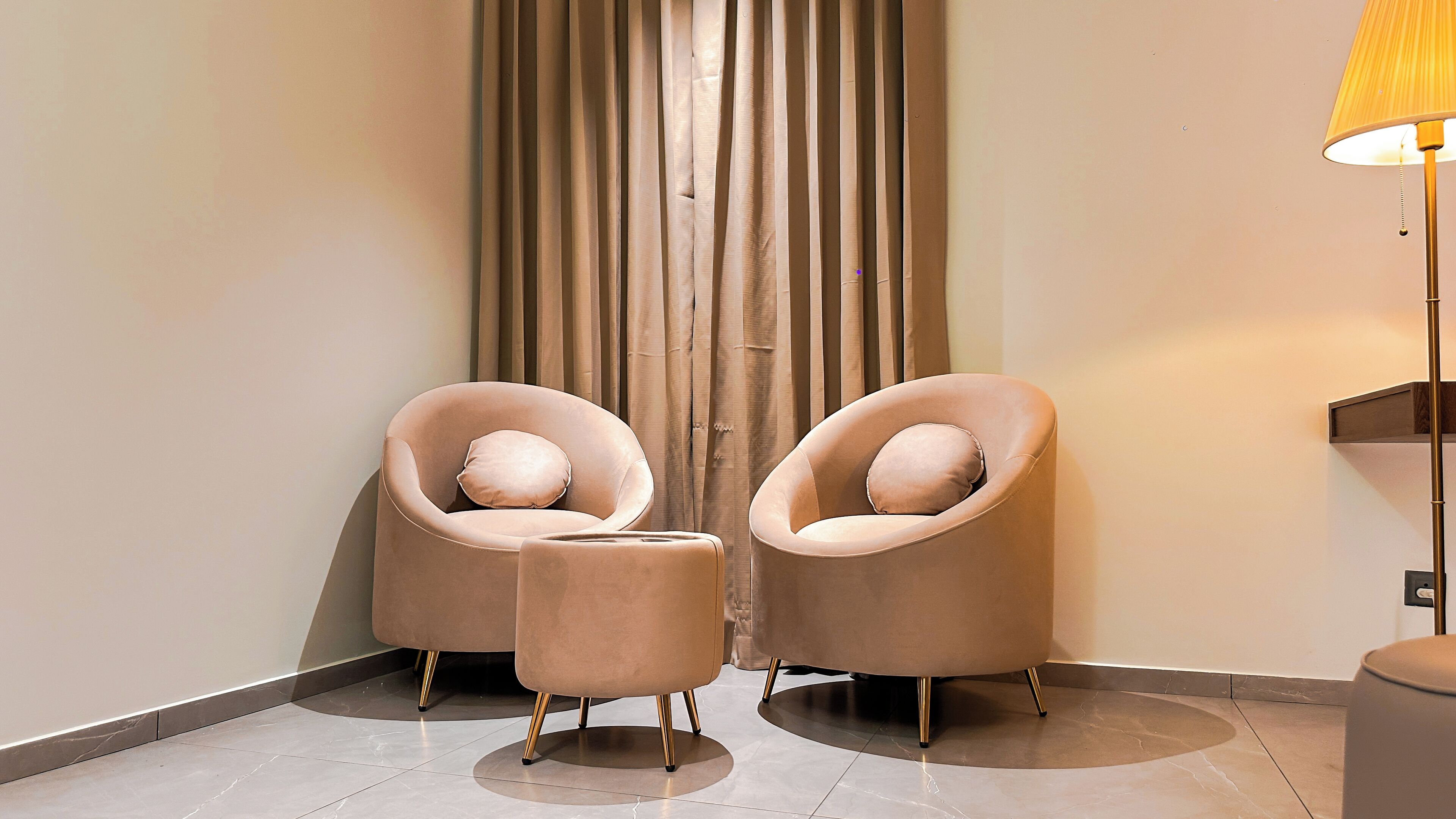 A modern room with two armchairs and a small ottoman, a floor lamp, and a curtain.