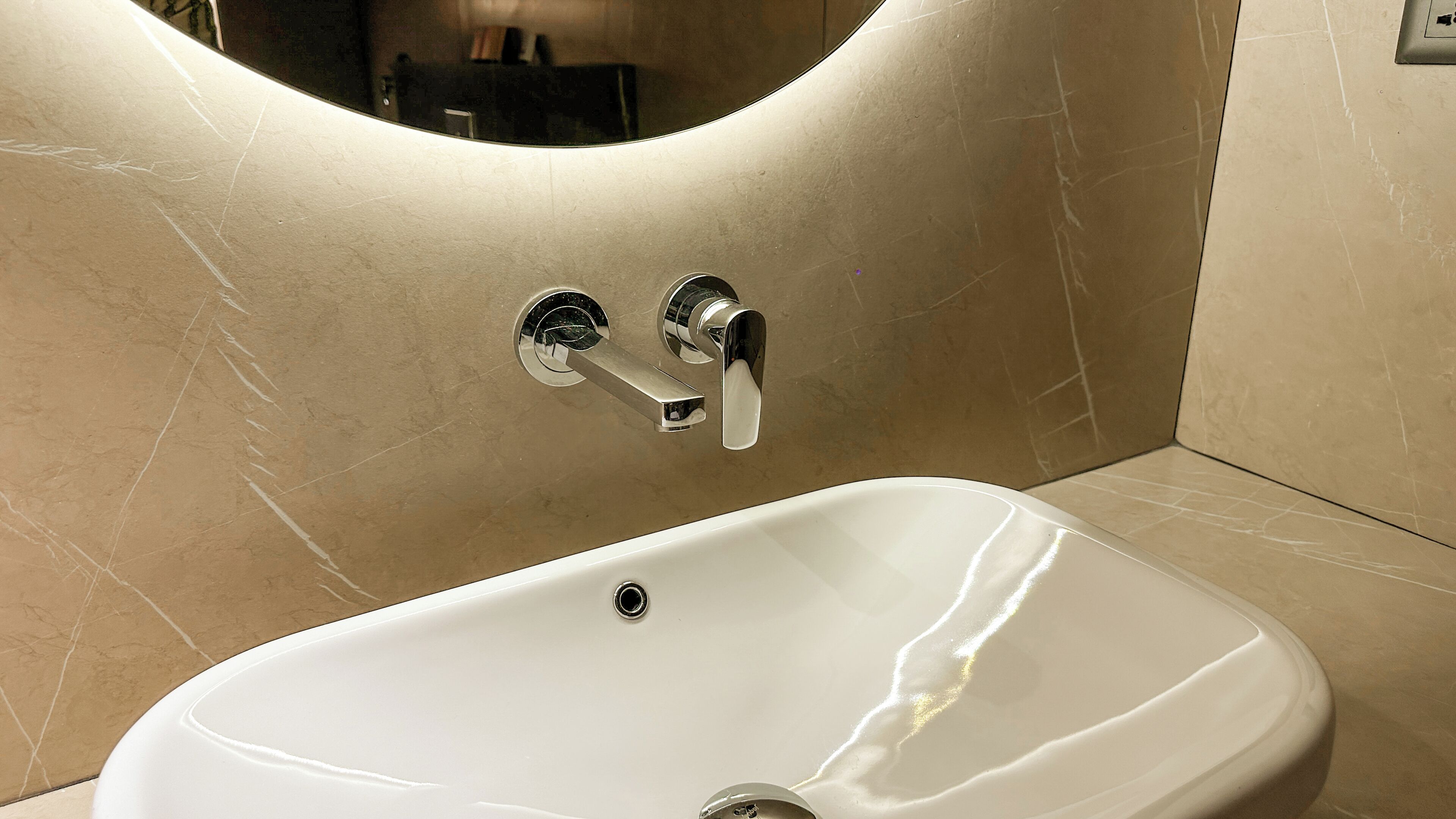 A bathroom with a white sink, chrome faucets, and a curved mirror above the sink.