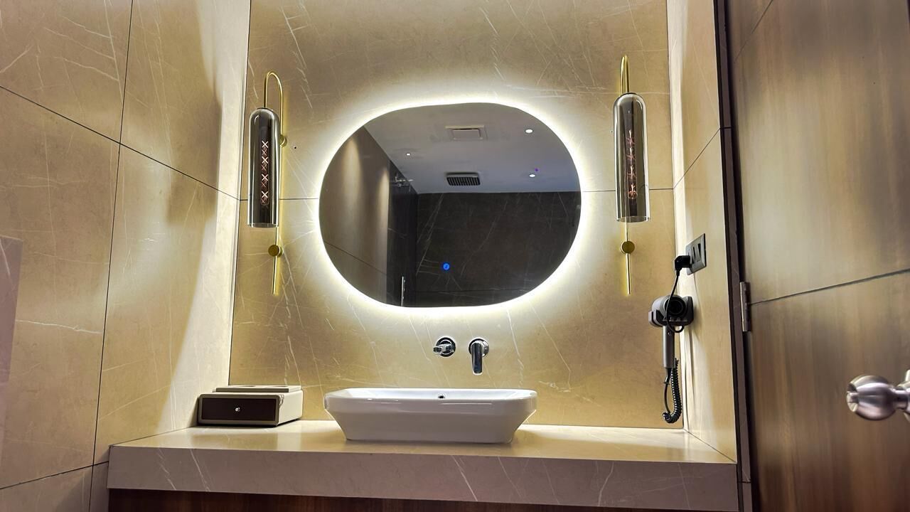 A modern bathroom with a round mirror, a white sink, and a handheld showerhead.