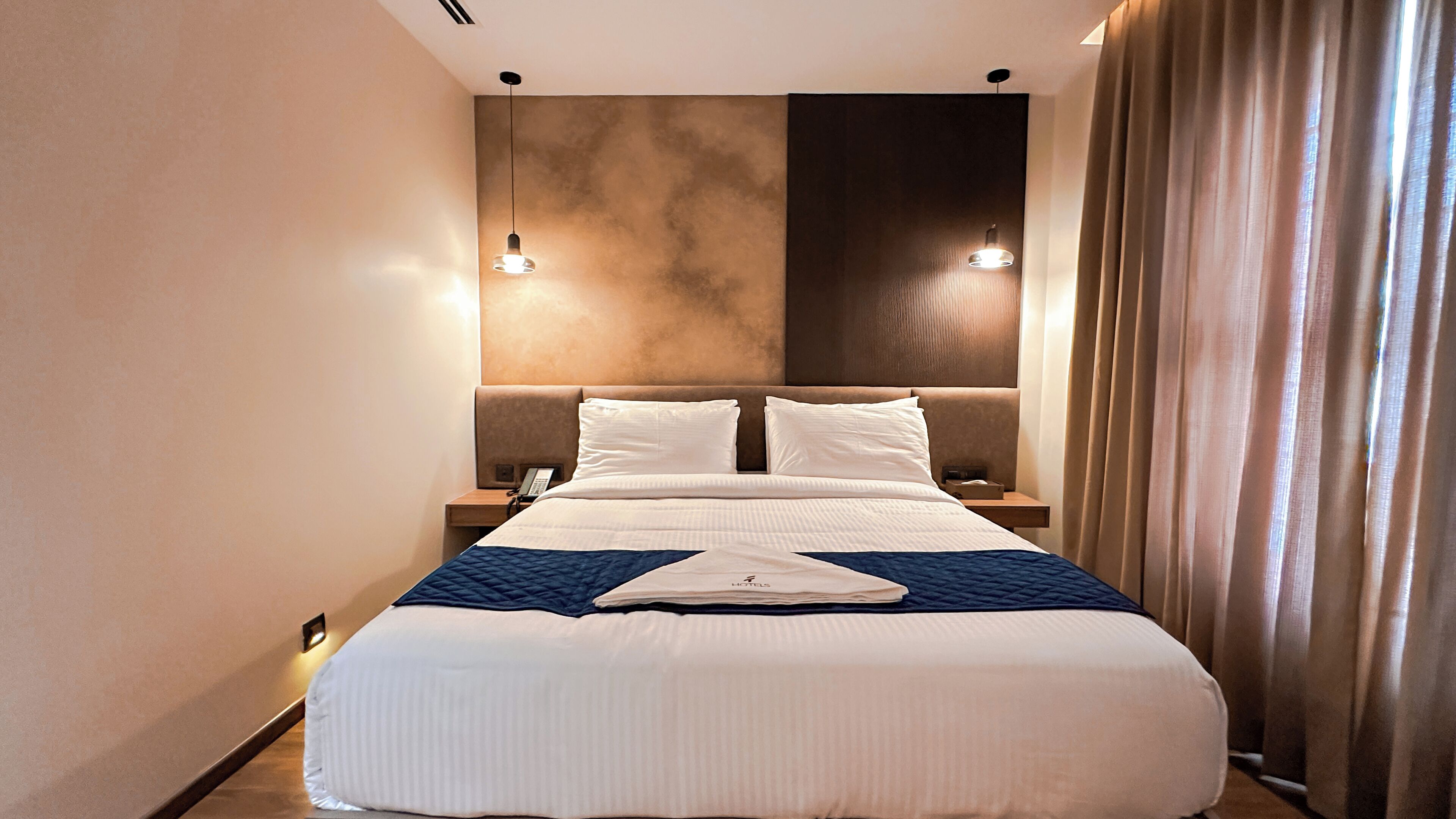A hotel room with a large bed, two bedside tables, a phone, and a nightstand.