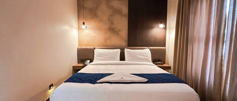 Quarto de hotel com uma cama grande, duas mesas de cabeceira, um telefone e um criado-mudo.