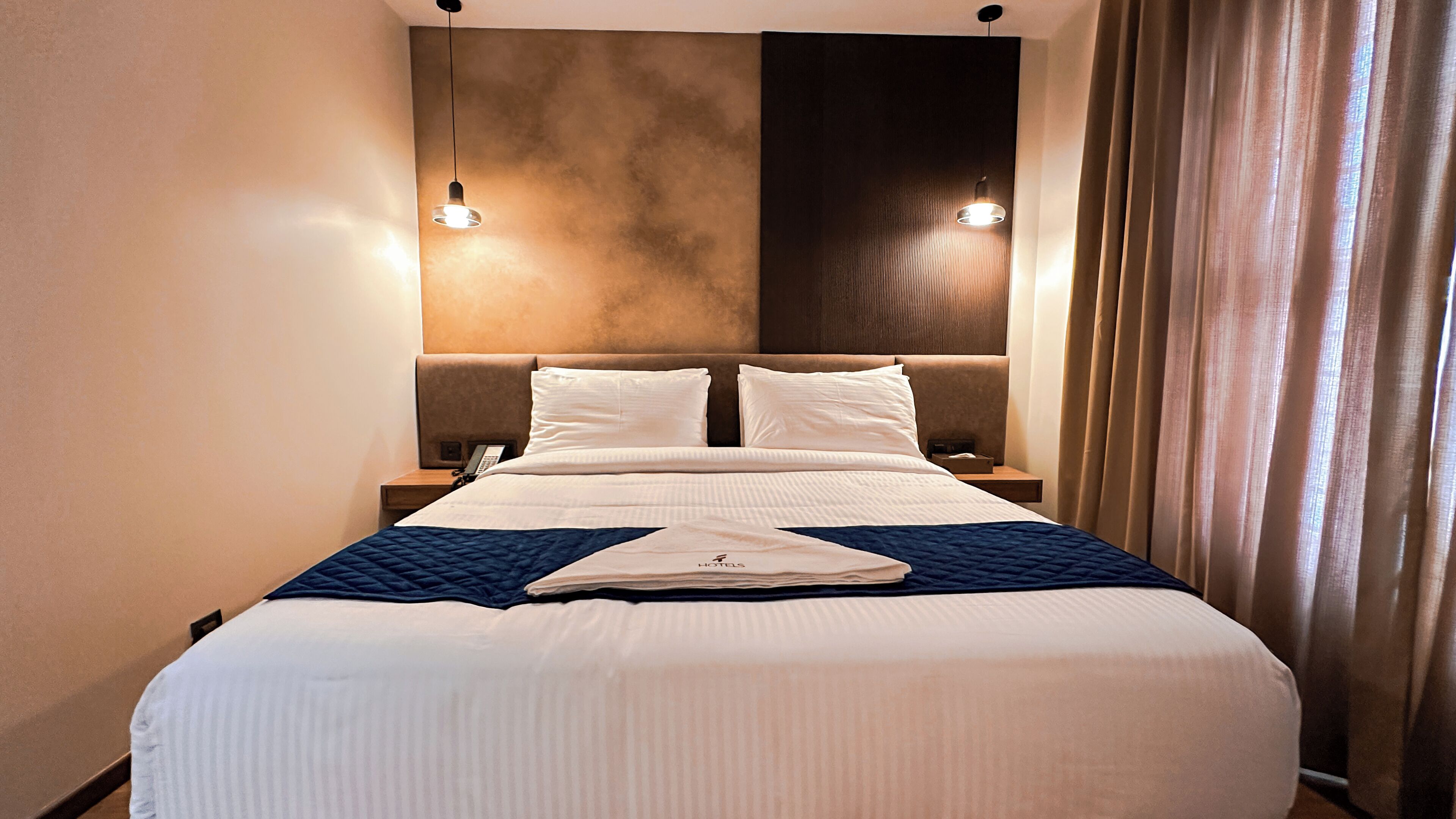 A hotel room with a large bed, two bedside tables, a headboard, and a wall-mounted light fixture.