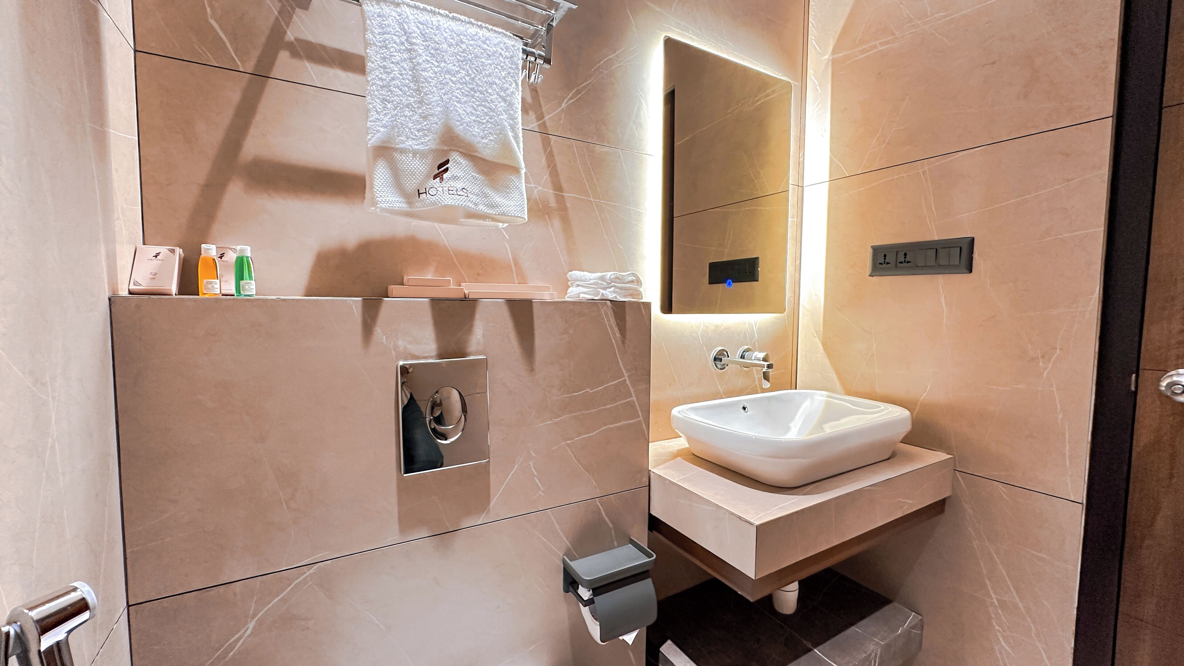 A modern bathroom with a marble sink, a towel rack, and toiletries on a shelf.