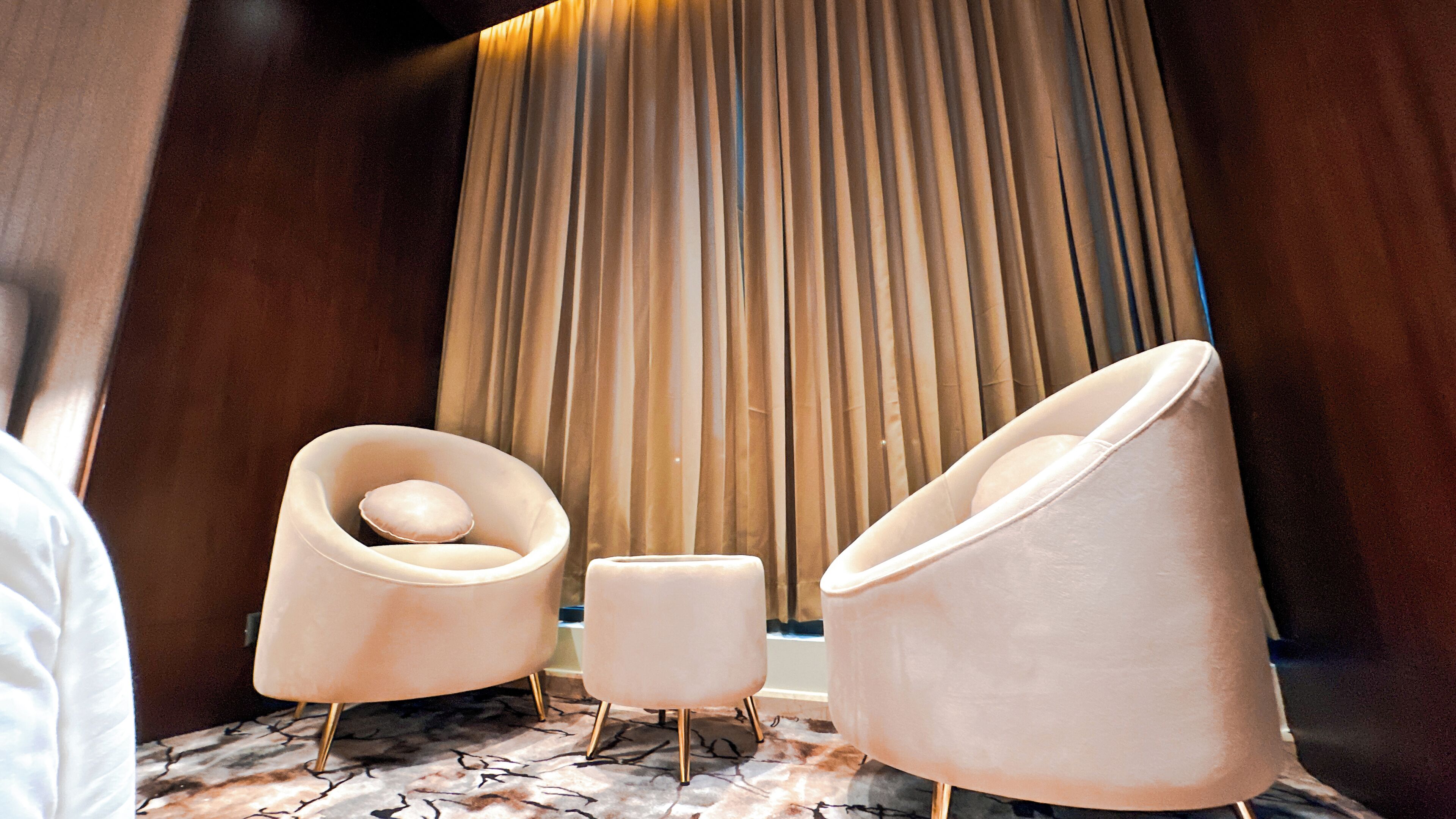 A modern room with two plush armchairs, a small ottoman, and a vertical wooden panel.