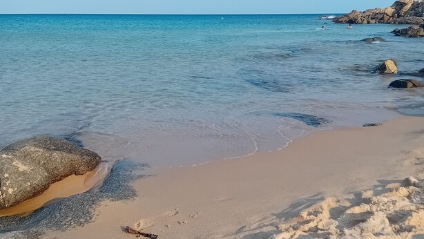 A beach with clear water, sandy shore, and rocky outcrops.