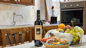 A bottle of wine, a basket of fruits, and cookies on a table in a kitchen.