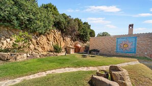 A stone wall with a mosaic, a stone building, and a grassy area with a path.