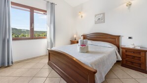 A bedroom with a wooden bed, a nightstand with a lamp, a wall clock, and a window with curtains.