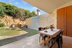 A patio with a table and chairs, a stone wall with a mosaic, and a view of a hillside.