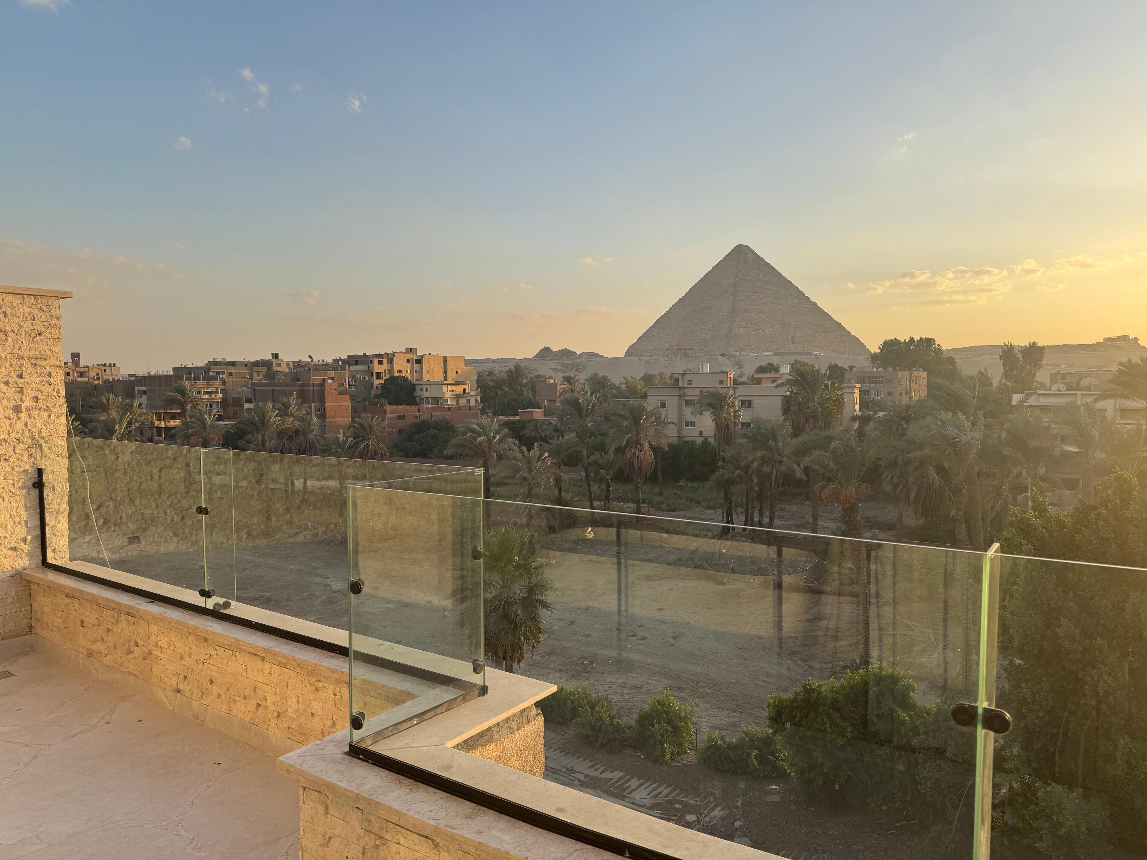 A view from a balcony with a glass railing overlooking a cityscape, including a pyramid and residential buildings.