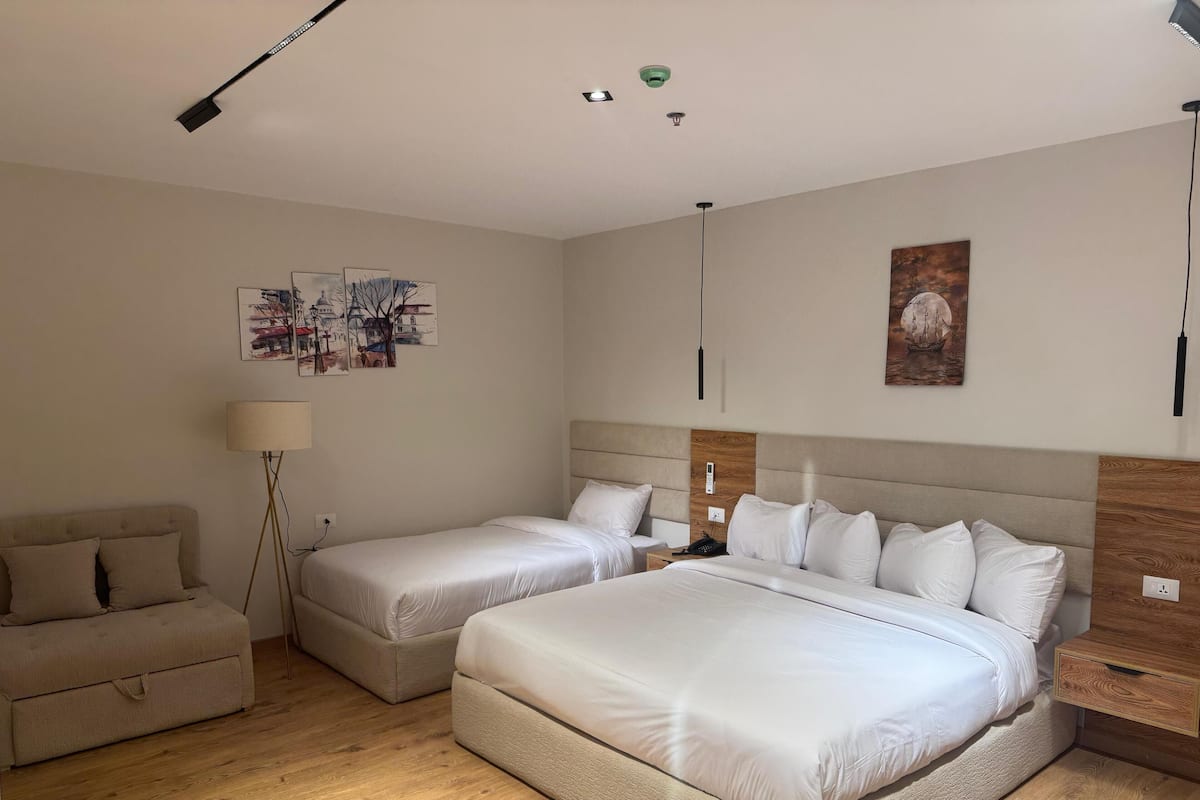 A hotel room with a large bed, a smaller bed, a sofa, a lamp, and artwork on the walls.
