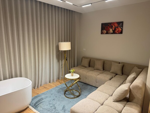 Ein modernes Wohnzimmer mit einem beigefarbenen Sofa, einem kleinen runden Tisch mit einer Lampe und einem blauen Teppich.