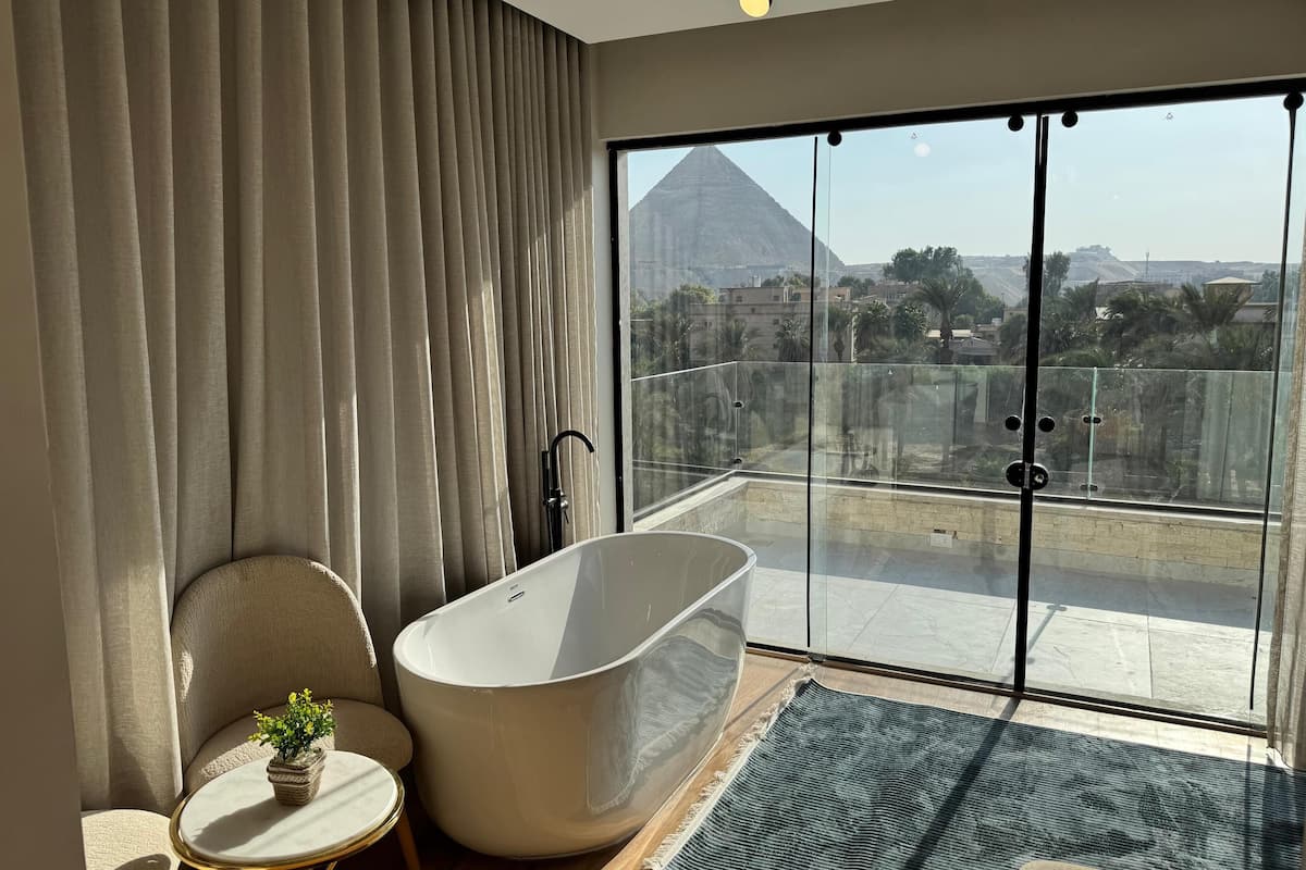 A modern bathroom with a freestanding bathtub, a round table with a plant, and a view of a pyramid through large glass doors.