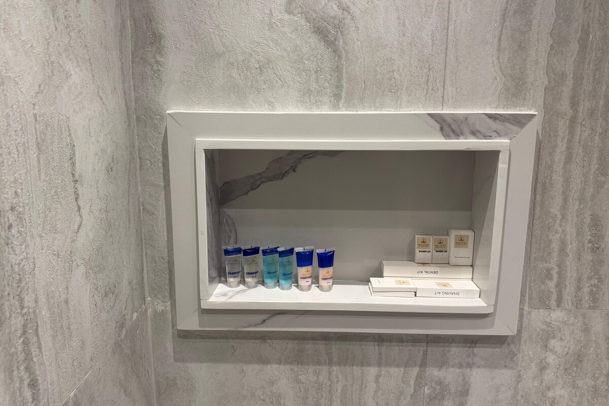 A bathroom with a marble wall and a shelf containing toiletries.