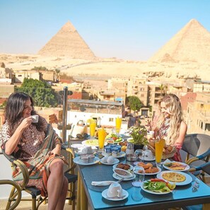 Two people seated at a table with a view of the pyramids, a variety of breakfast items, and a clear sky. - Palacio Pyramids Hotel (Giza)