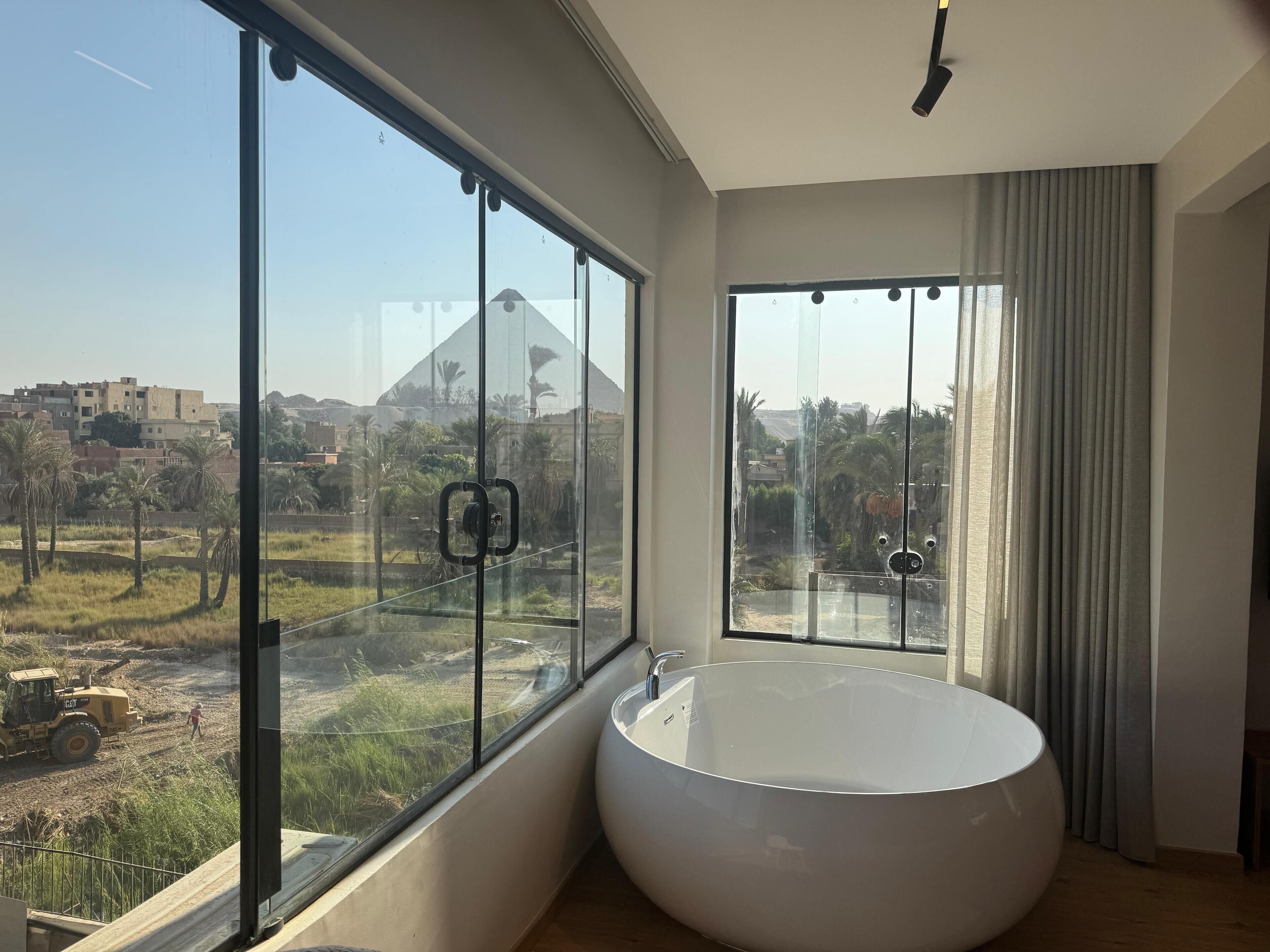 A modern bathroom with a large bathtub, large windows, and a view of a construction site.