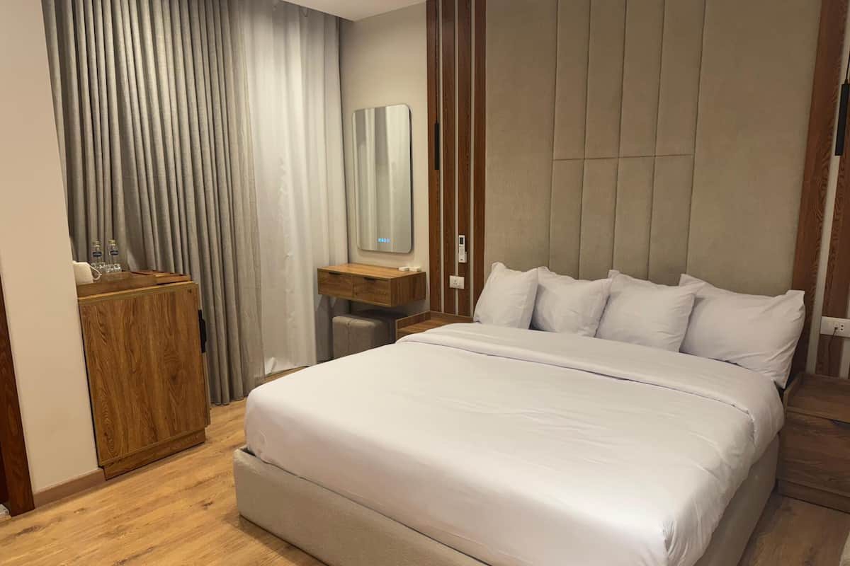 A modern hotel room with a large bed, wooden wardrobe, and a vanity with a mirror.