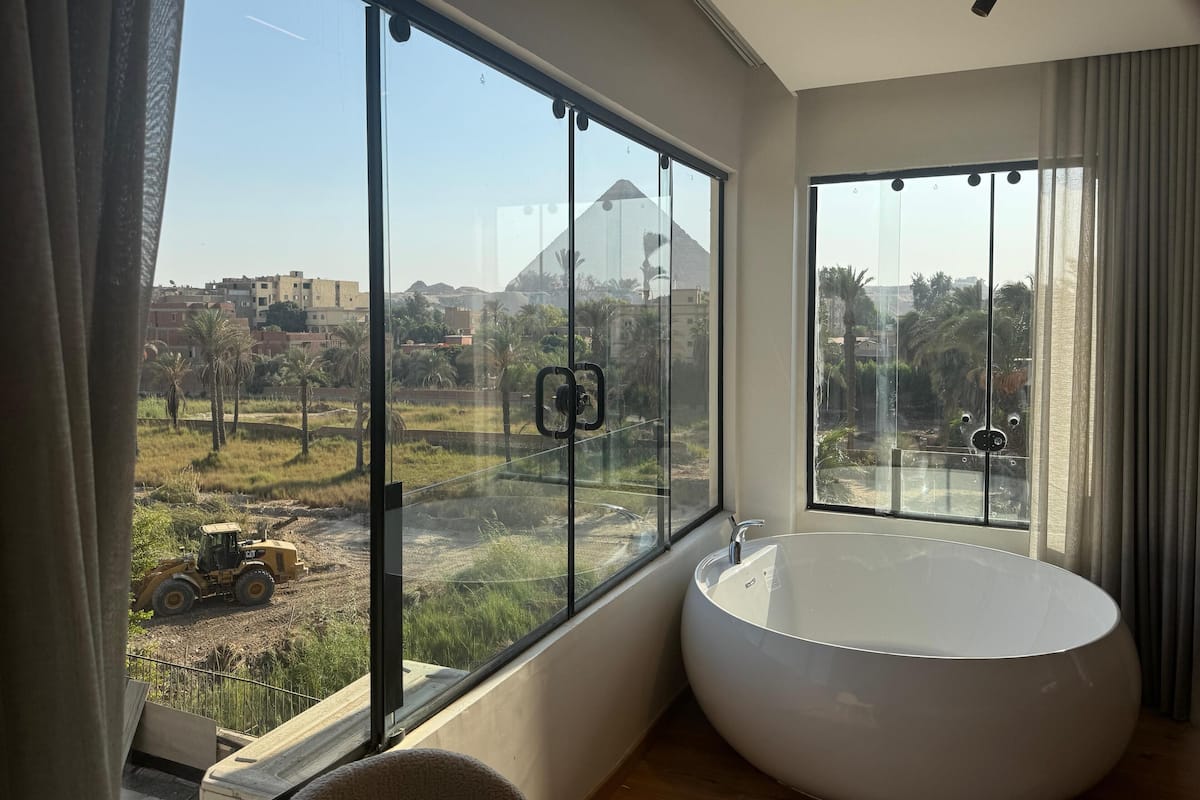 A modern bathroom with large windows, a large bathtub, and a view of a construction site.
