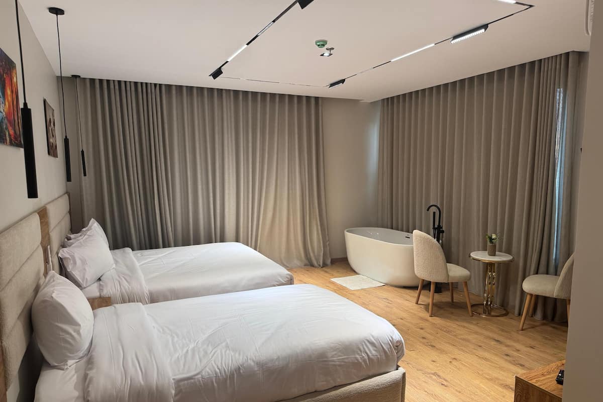 A modern hotel room with two large beds, a bathtub, a small round table, and a chair.
