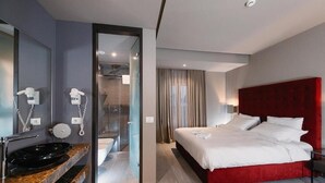 Una camera d'albergo moderna con una testiera rossa, un lavandino nero e un box doccia in vetro.