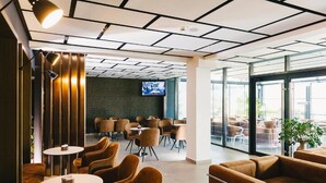 Un interno moderno con diverse zone relax, tra cui tavoli rotondi e divani, e un televisore fissato alla parete.