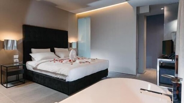 Una camera d'albergo moderna con un letto grande, una vasca da bagno bianca con petali di rosa e un piccolo comodino.