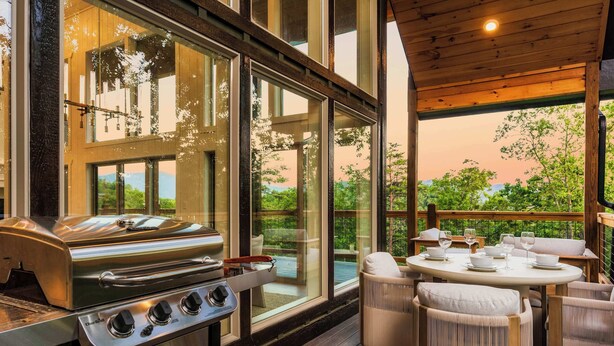 A modern outdoor kitchen with a stainless steel grill, large windows, and a wooden deck. - Luxe Home - Heated Pool, Hot Tub & Mountain Views! (Sevier County)