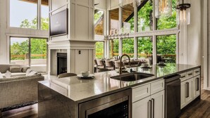 A spacious kitchen with a large island, a fireplace, and large windows offering a view of the outdoors. - Luxe Home - Heated Pool, Hot Tub & Mountain Views! (Sevier County)