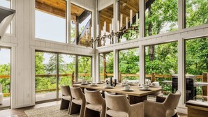 A spacious dining area with a long table set for six, surrounded by large windows offering a view of lush greenery. - Luxe Home - Heated Pool, Hot Tub & Mountain Views! (Sevier County)