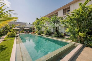 A swimming pool surrounded by lush greenery and a building with multiple balconies. - Sari Uma Canggu By Hospitality Bali (Canggu)