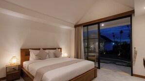 A modern bedroom with a large bed, bedside lamps, and a view of a tropical landscape through a sliding glass door. - Sari Uma Canggu By Hospitality Bali (Canggu)
