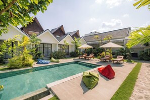 A modern outdoor pool area with lounge chairs and umbrellas, surrounded by lush greenery and a well-maintained lawn. - Sari Uma Canggu By Hospitality Bali (Canggu)