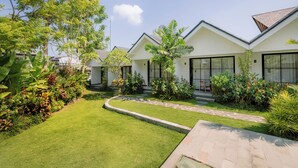 A modern hotel with white exterior walls, large windows, and a well-maintained garden with various plants and a paved pathway. - Sari Uma Canggu By Hospitality Bali (Canggu)
