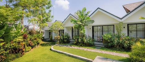 A modern hotel with white exterior walls, large windows, and a well-maintained garden with various plants and a paved pathway.