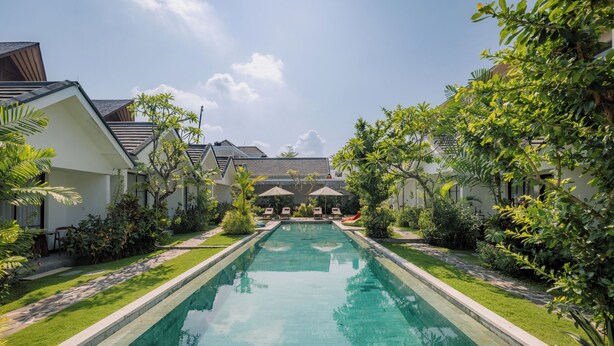 A rectangular swimming pool with a clear blue water surface, surrounded by a well-maintained lawn and various tropical plants. - Sari Uma Canggu By Hospitality Bali (Canggu)