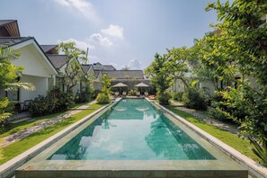 A rectangular swimming pool with a clear blue water surface, surrounded by a well-maintained lawn and various tropical plants. - Sari Uma Canggu By Hospitality Bali (Canggu)