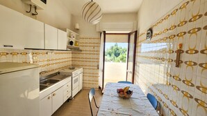 A compact kitchen with white cabinets, a sink, and a dining table with a fruit basket. - Casa Bianca Villaputzu (Villaputzu)