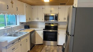 Una cocina compacta con armarios blancos, horno de acero inoxidable, microondas y refrigerador.