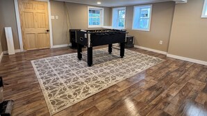 Una habitación amplia con mesa de billar, suelo de madera y ventanas grandes.