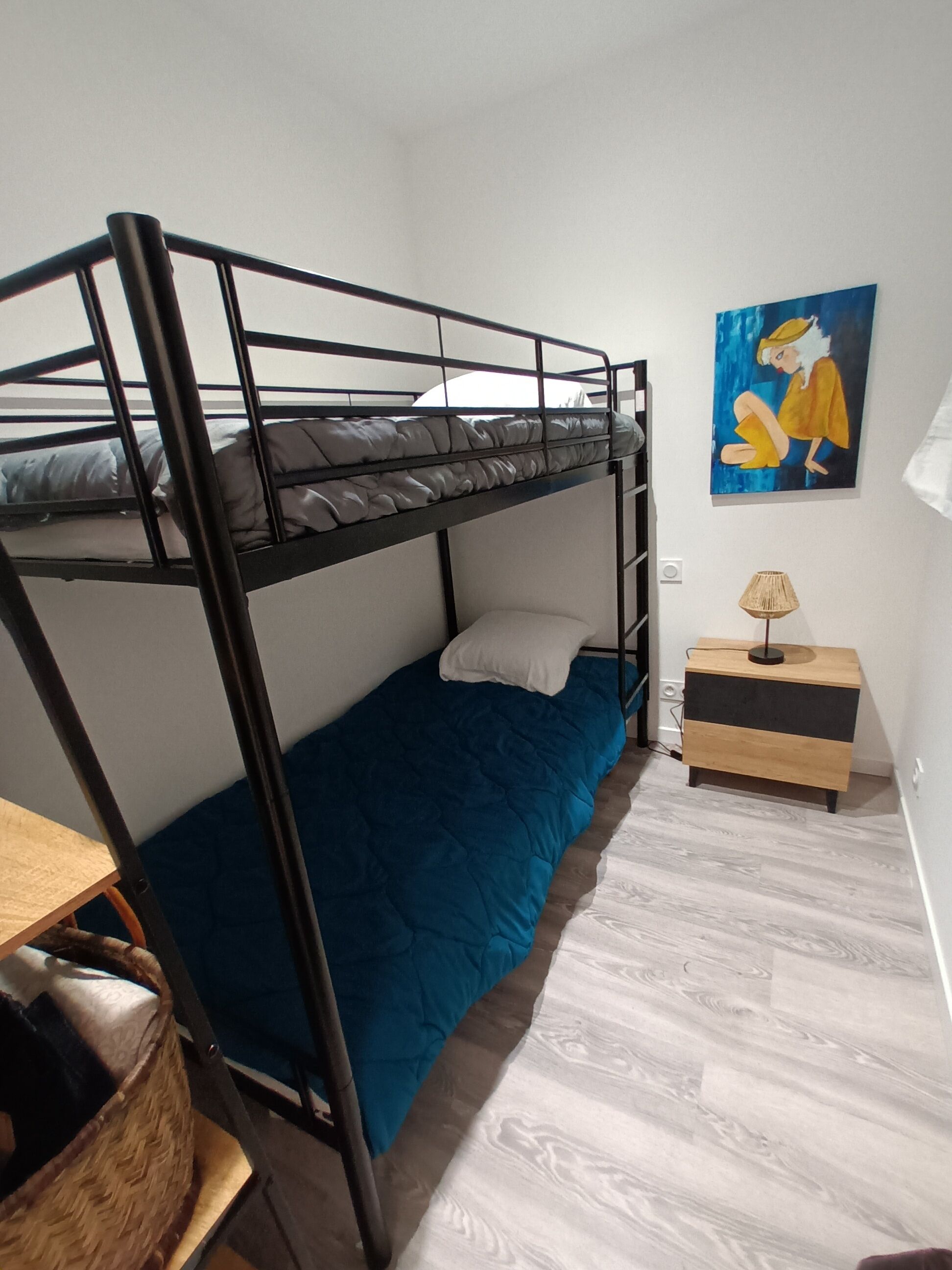 Camera con letto a castello, materasso blu, un comodino di legno e un quadro appeso al muro.