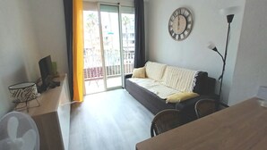 Un salon comprenant un canapé, une table à manger, un ventilateur, une horloge et une vue sur l’extérieur, accessible par une porte coulissante.