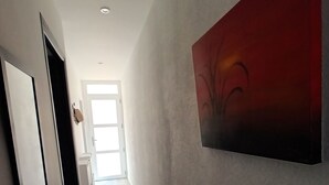 Un couloir avec une porte sur la gauche, une fenêtre au fond et un tableau abstrait rouge sur le mur de droite.