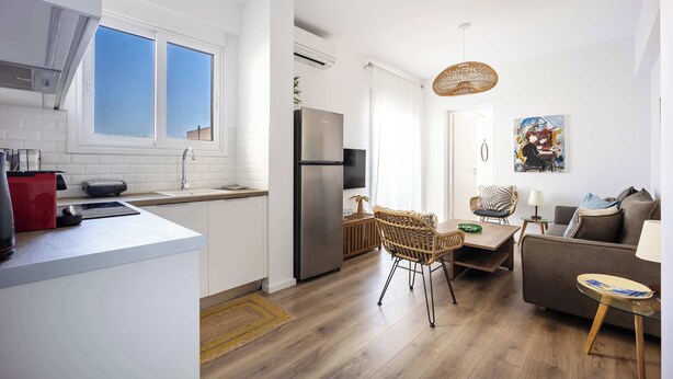 A modern kitchen with white cabinets, a stainless steel refrigerator, and a dining area with wicker chairs and a glass table. - Bright Stylish 2BR | Acropolis View Balcony | King Bed (Athina)