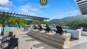 A rooftop terrace with lounge chairs, a hot tub, and a pool overlooking a mountainous landscape. - New 1 BR Condo - Rooftop Pool - Oceanview (Puerto Vallarta)