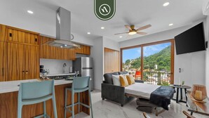 A modern kitchen with wooden cabinets, a stainless steel refrigerator, and a bar area with two stools. - New 1 BR Condo - Rooftop Pool - Oceanview (Puerto Vallarta)