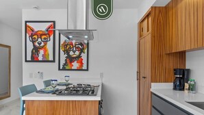 A modern kitchen with a gas stove, wooden cabinets, and two framed animal paintings on the wall. - New 1 BR Condo - Rooftop Pool - Oceanview (Puerto Vallarta)