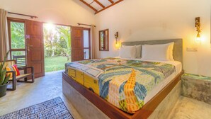 Une chambre à coucher avec un grand lit, une tête de lit en bois et une vue sur le jardin par une porte ouverte.