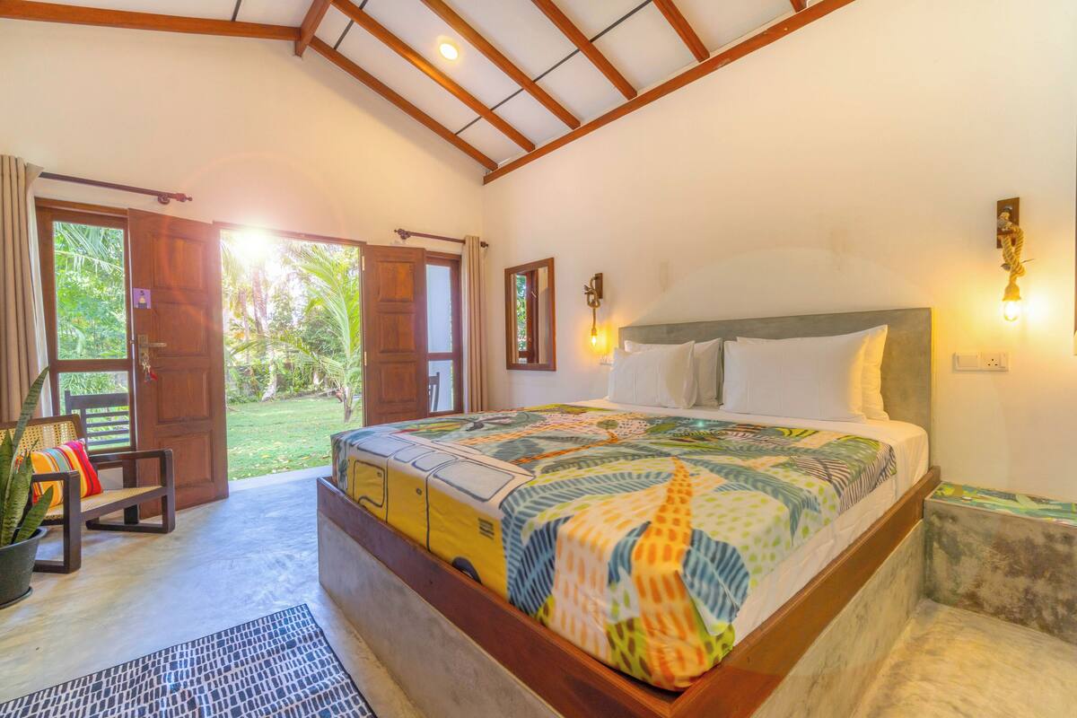 A bedroom with a large bed, wooden headboard, and a view of the garden through an open door.