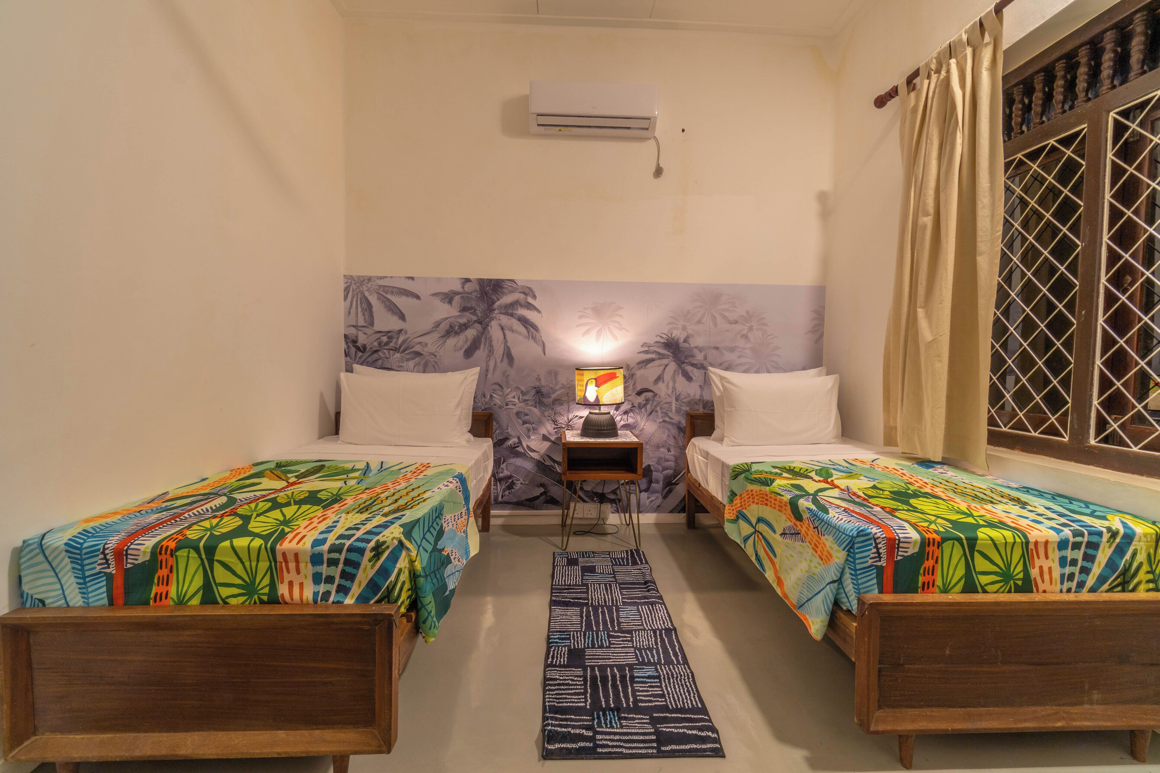 A room with two beds, a nightstand, a wall-mounted air conditioner, and a window with a curtain.