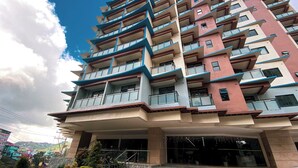 A multi-story building with balconies, a stone base, and a clear sky. - Premium Couple Room with Balcony at Megatower (Baguio)